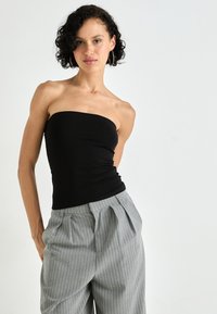 Top nero senza spalline in un design aderente, abbinato a pantaloni grigi chiari a righe sottili con pieghe e una silhouette rilassata.