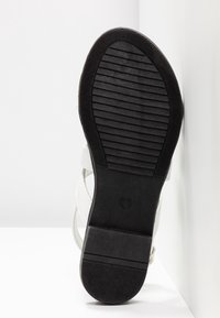 Sandale blanche avec une semelle en caoutchouc noir texturé, équipée de fines lanières et d'un design simple. Taille indiquée comme 37.