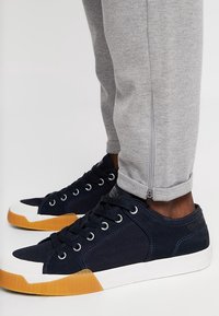 Granatowe tenisówki z płócienną cholewką i białym noskiem oraz gumową podeszwą, zestawione z szarymi dresami z zamkiem przy kostce.