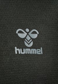 Stiliseret hvid bi-logo over ordet "hummel" på sort tekstureret stof, der repræsenterer Hummel sportsmærke.