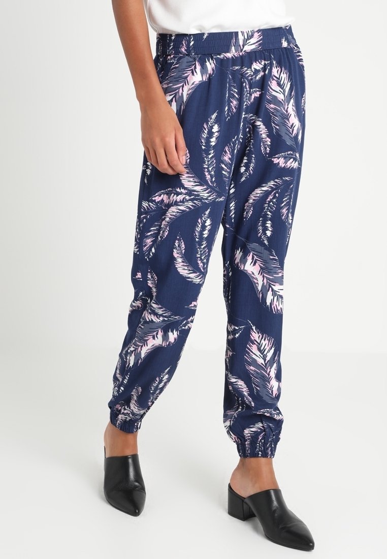 Vêtements pour jambes avec motif de plumes bleu marine et rose, taille élastique et poignets, portés avec des chaussures noires à talons slip-on.