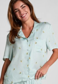 Lichtblauw geruit overhemd met korte mouwen, gele bloemaccenten, knoopsluiting en een borstzak; gladde stof met een relaxte pasvorm.