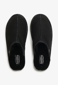 Zapatillas negras sin cordones con un suave forro de felpa, detalles cosidos y borde con marca. El material exterior es liso, con un interior acogedor.