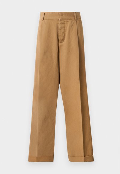 Pantalons larges marron clair avec passants de ceinture, fermeture éclair frontale et ourlets à poignets sur un fond blanc uni.