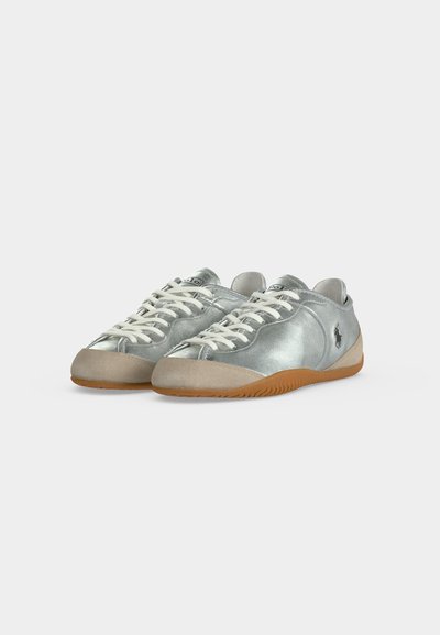 Paire de baskets basses argentées avec des lacets blancs, des embouts beige, des semelles en gomme et un petit logo sombre sur les côtés extérieurs.