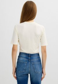 Camiseta de manga corta color crema con cuello redondo, combinada con unos pantalones vaqueros de talle alto azules que presentan bolsillos traseros y una silueta ajustada.