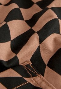 Hnedo-čierna kockovaná látka s hladkou textúrou, ktorá má vlnitý vzor a viditeľné prešívanie pozdĺž okrajov.