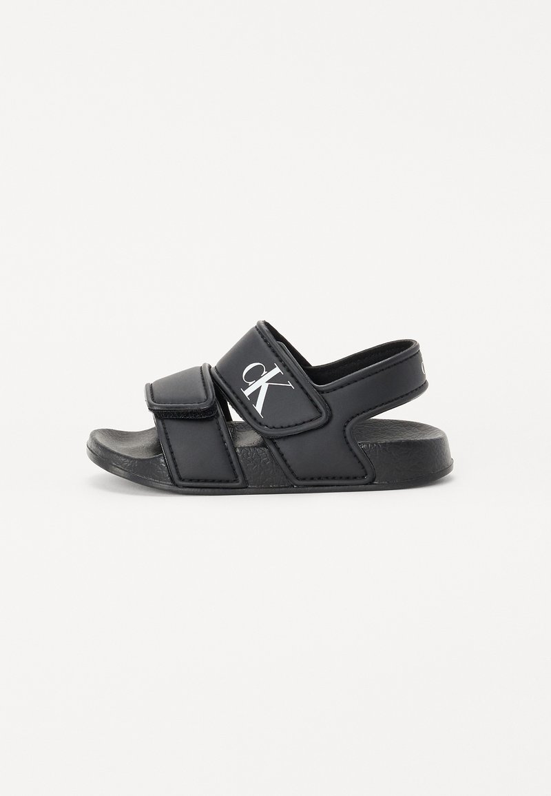 Black sandals with two adjustable Velcro straps, textured synthetic upper, and a flat, contoured rubber sole featuring a small logo.