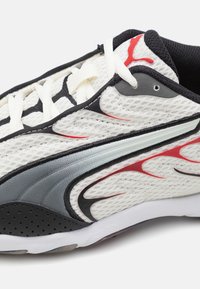 Chaussures de sport en maille blanche avec des motifs de flammes rouges et noires, des superpositions grises et une semelle en caoutchouc noir avec des perforations. Les lacets sont blancs.