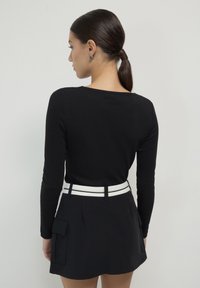 Haut noir à manches longues associé à une jupe noire avec des poches latérales et une ceinture blanche, mettant en avant un design ajusté et une texture lisse.