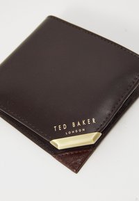 Bruine leren portemonnee met een gladde textuur, voorzien van metallic gouden branding en een hoekige gouden accent in de hoek.