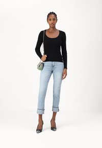 Svart langermet tettsittende topp i kombinasjon med lyseblå cropped jeans. Modellen holder en liten grønn rutete håndveske og har på seg svarte spisse hæler.