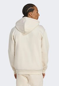 Sudadera con capucha de color crema, confeccionada en un tejido suave, con detalles de costura y un corte relajado. La vista trasera muestra la capucha y los puños acanalados.