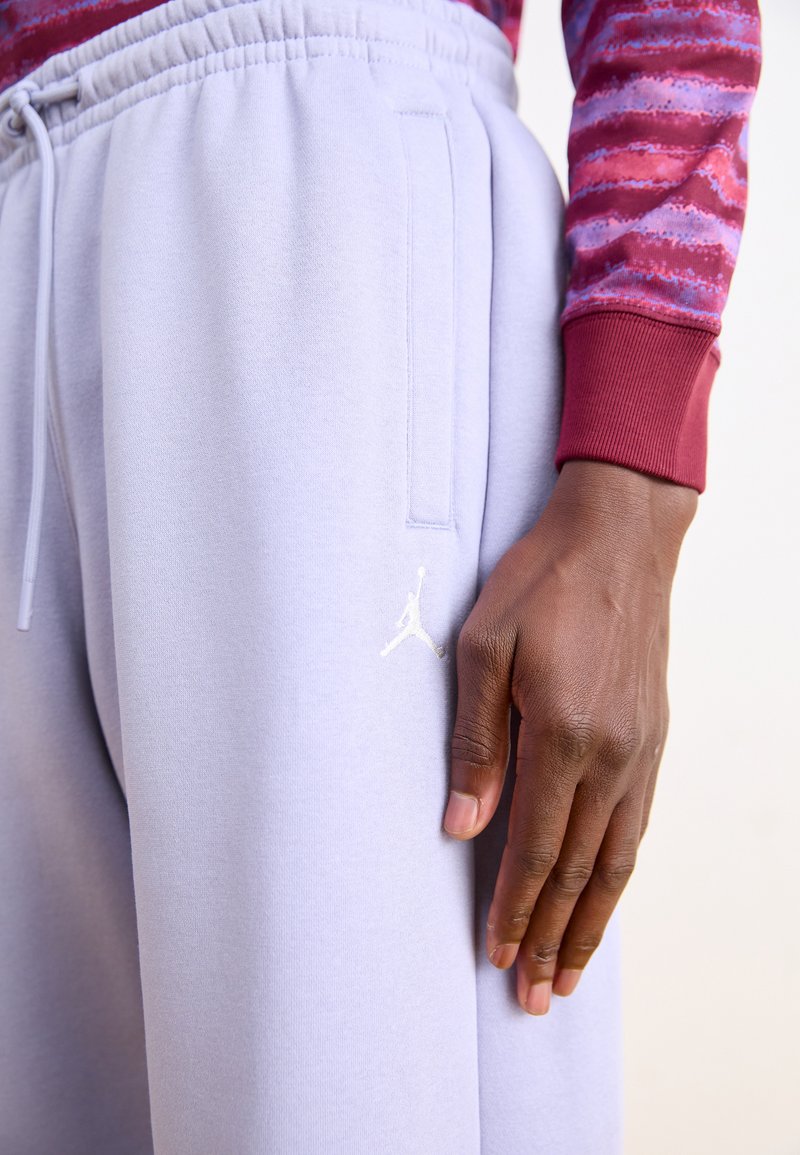 Pantalons de survêtement violet clair en tissu doux avec taille élastique, poches latérales et logo Jumpman brodé en blanc sur la cuisse gauche.