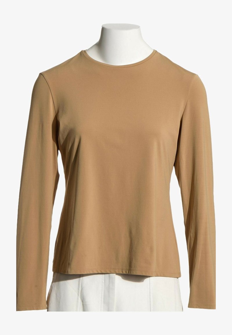 Chemise beige à manches longues et col rond sur un buste de mannequin avec un pantalon blanc sur fond blanc uni.