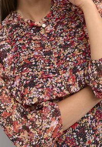 Hedvábná blůza s květinovým vzorem, lehká s volánkovou texturou v odstínech červené, růžové a černé, se zapínáním na knoflík u krku a balónovými rukávy.