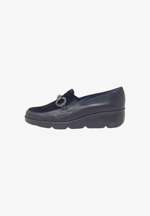 Scarpa nera slip-on realizzata in materiali scamosciati e in pelle liscia, con punta rotonda, suola a cuneo chunky e un accento decorativo in metallo.