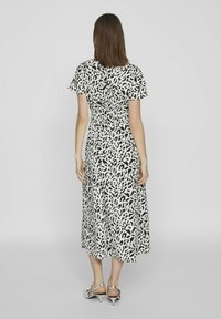 Czarna i biała sukienka midi w zwierzęcy wzór z krótkimi rękawami, smockowanym pasem i rozkloszowanym dołem. Modelka nosi srebrne sandały na obcasie.