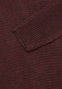 Gros plan sur un tissu tricoté marron texturé, montrant la manche et le corps principal d’un pull en grosse laine.