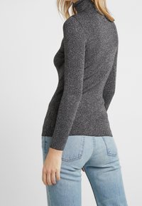 Grå ribbad turtlenecktröja med en subtil lyster, tillverkad av ett texturerat tyg; smal passform, långa ärmar och hög krage.