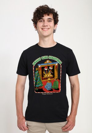 T-shirt noir avec un graphisme coloré et festif représentant des enfants près d'une cheminée, un sapin de Noël, et le texte "Ça sent Noël".