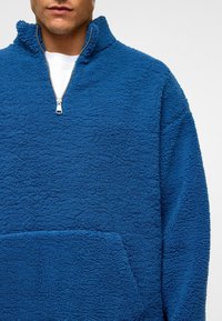 Fleece pullover in helderblauw met een gestructureerd oppervlak, half-rits kraag en een voorkantvak voor extra functionaliteit.