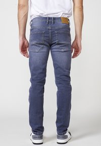 Jeans ajustados de mezclilla azul oscuro con una cintura de altura media, dos bolsillos traseros con detalles de costura y un parche de cuero marrón claro en la cinturilla.