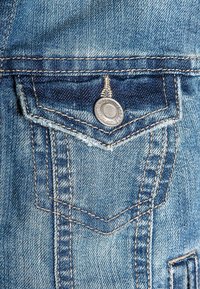 Jeans tyg blå ficka med en metallknapp, synliga stygn och en klassisk design med en strukturerad yta.