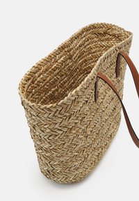 Sac fourre-tout en paille tissée avec des poignées en cuir marron. Présente un design à ouverture supérieure et une surface texturée avec des variations de couleur naturelles.