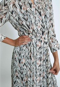 Abito button-up in tessuto leggero con un motivo astratto a zigzag nei colori nero, beige e bianco, con vita cinchata e maniche lunghe.