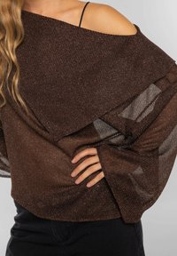 Top marrón semi-transparente con textura brillante, diseño hombros caídos y mangas anchas. Tela con capas que añade profundidad e interés visual.