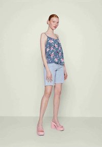 Blomstermønstret blå top, lyseblå shorts og pink platform sandaler. Glat stof, løs pasform, tynde stropper og bred nederste kant.