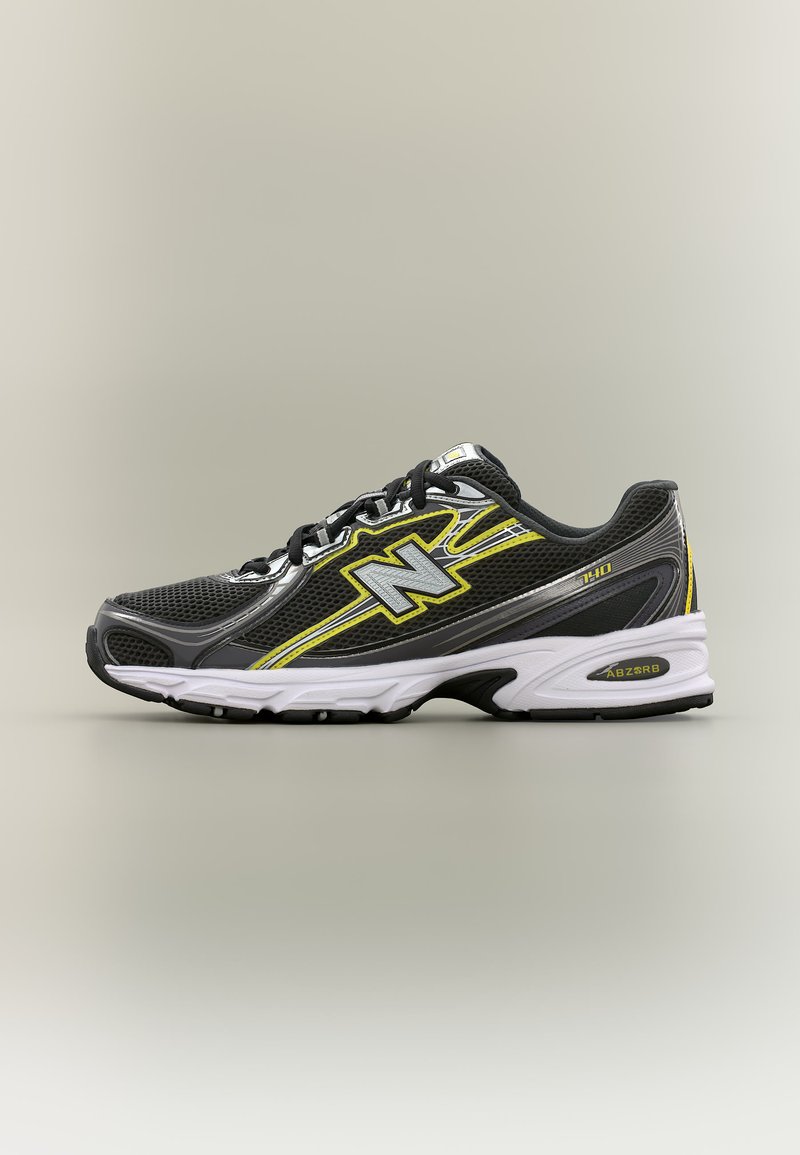 Μαύρο και γκρι αθλητικό παπούτσι New Balance με κίτρινες λεπτομέρειες, μαύρα κορδόνια και λευκή σόλα σε απλό μπεζ φόντο.