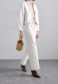 Chaqueta de mezclilla blanca y pantalones combinados con zapatos de tacón marrones. Un bolso de paja trenzada con asas de cuero completa el atuendo.