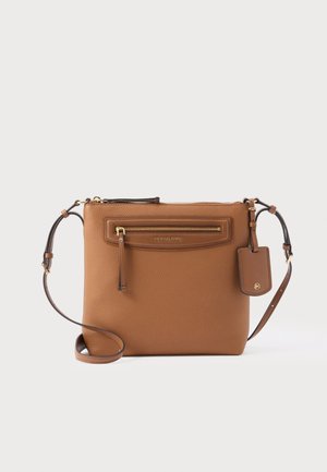 Sacoche en cuir marron avec poche avant zippée, bandoulière réglable et étiquette logo suspendue sur fond blanc.