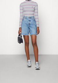 Haut à manches longues rayé aux tons pastel ; short en denim taille haute avec bords effilochés ; baskets grises ; portant un petit sac à main noir.