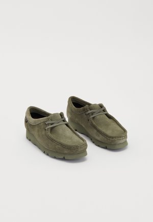 Green suede shoes with a rounded toe and lace-up design. Features a thick rubber sole and stitched detailing along the upper.