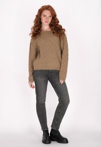 Bézs kötött pulóver gyémántmintával, laza fazonban, bordázott mandzsettákkal, sötétszürke skinny farmernadrággal és fekete vastag talpú bokapaneles csizmával párosítva.