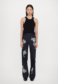 Zwart mouwloos topje gecombineerd met donkere denim jeans met witte bloemenborduursels, rechte pijpen en een tailleband met lussen voor een riem.