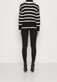 Pull en maille rayé noir et crème à col roulé, avec manches longues et coupe ample. Associé à des leggings noirs et des bottines.