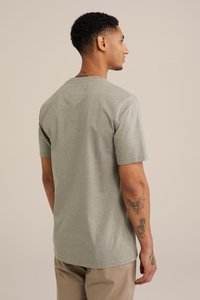 Gai pelēks īsām piedurknēm T-kreklis, ar apaļu kakla izgriezumu, brīva piegriezuma, mīksta tekstūra, smalka hetra raksts, valkāts kopā ar bēšiem biksēm un redzamām tetovējumiem uz rokas.