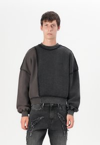 Sudadera de forro polar en gris oscuro con cuello redondo, corte oversize y costuras texturizadas. Combinada con jeans grises desgastados que presentan detalles deshilachados.