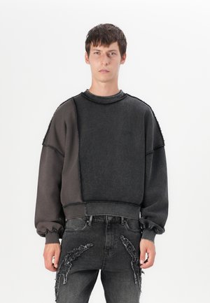 Sudadera de forro polar en gris oscuro con cuello redondo, corte oversize y costuras texturizadas. Combinada con jeans grises desgastados que presentan detalles deshilachados.