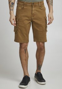 Brown cargo shorts made of cotton with a smooth texture, featuring side pockets, a slim fit, and stitched hems. Worn with black sneakers.