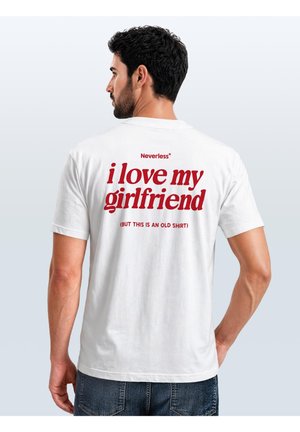 Mann, der von hinten zu sehen ist und ein weißes T-Shirt mit rotem Text trägt, auf dem "i love my girlfriend (but this is an old shirt)" steht, sowie blaue Jeans.