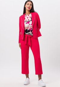 Bright pink blazer with silver zippers, paired with matching high-waisted cropped pants. Underneath, a patterned top featuring hearts and tigers.
