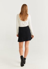 Jupe en tweed noir avec un design évasé, assortie à un haut blanc à manches longues ajusté. Le modèle porte des bottines noires.