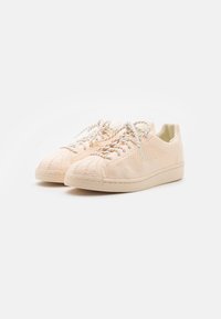 Baskets beige en maille avec une tige texturée et des lacets de couleur claire, dotées d'un design bas et d'un marquage subtil sur le talon.