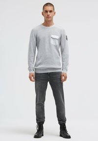 Hellgraues Langarmhemd aus strukturiertem Stoff mit Brusttasche, kombiniert mit dunkelgrauer Jeans und schwarzen Schnürstiefeln.