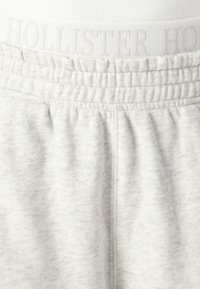 Light gray sweatpants feature an elastic waistband with embossed "HOLLISTER" logo, soft texture, and slightly tapered leg design.